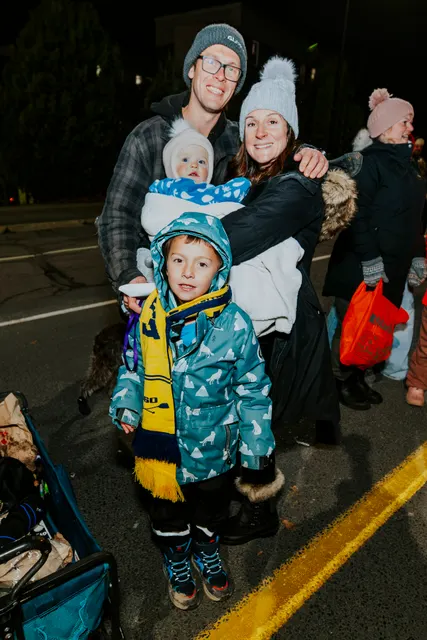 A family bundled in winter coats poses together at the parade at night.