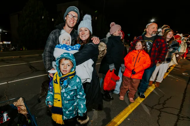 A family poses together as a line of spectators bundled in winter coats stretches behind them.