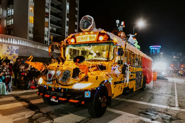 A yellow school bus decorated as a spooky Halloween-themed float, lit up with skeleton figures and candy cane trim.