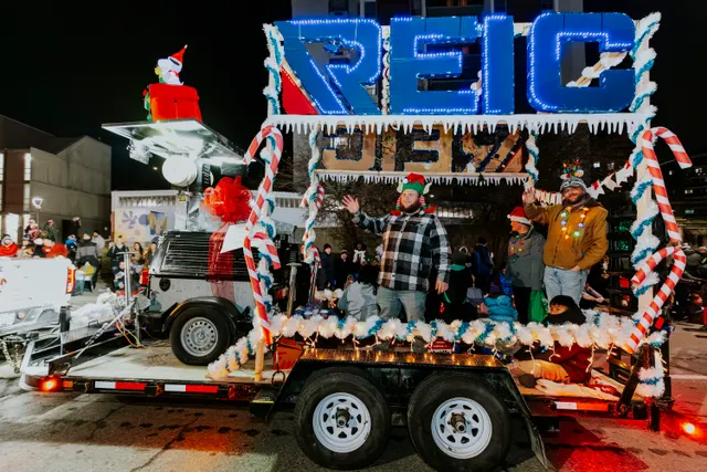 People wave from a float lit with a large sign and candy-cane poles in the parade.