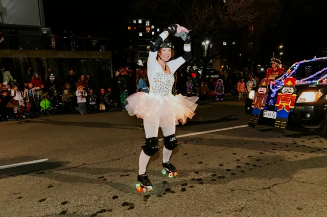 A skater in a light-up white tutu dances down the street past a toy-soldier-themed float.