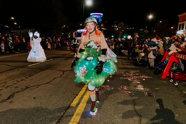 A skater in a glowing green dress rolls down the street as papers scatter behind her.