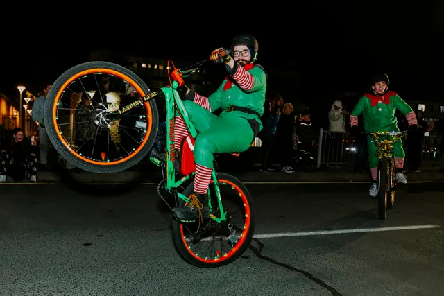 Two riders in elf costumes perform wheelies on bikes down the parade route.