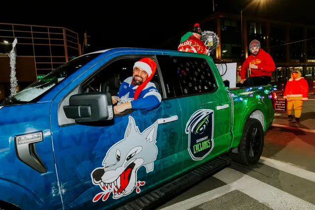A driver in a Santa hat waves from a truck decorated with a Sudbury Cyclones wolf logo.