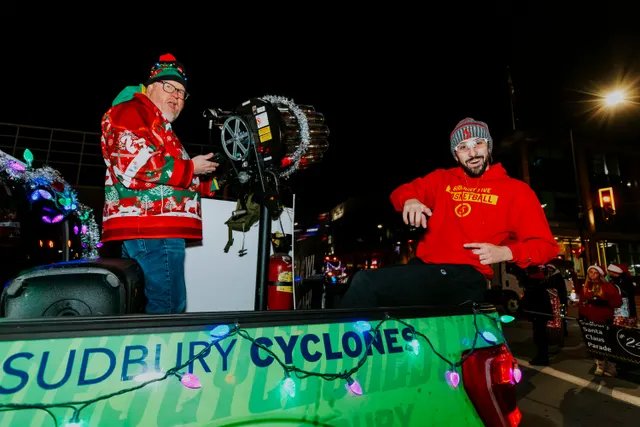 Two men stand on a Sudbury Cyclones float decorated with lights and a film-reel prop.