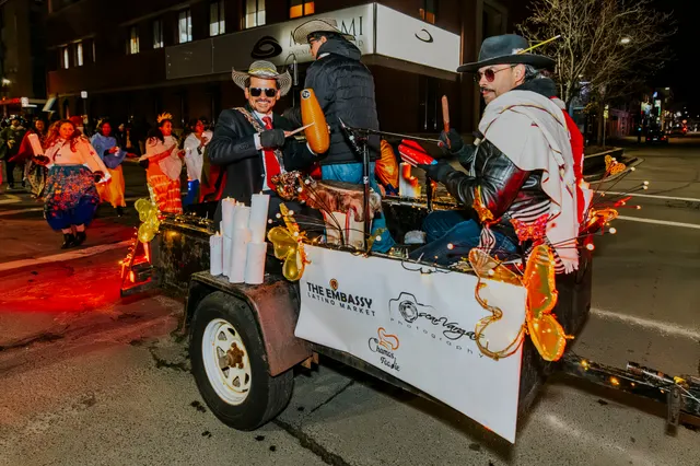 Performers in hats and sunglasses ride a trailer decorated for The Embassy Latino Market.