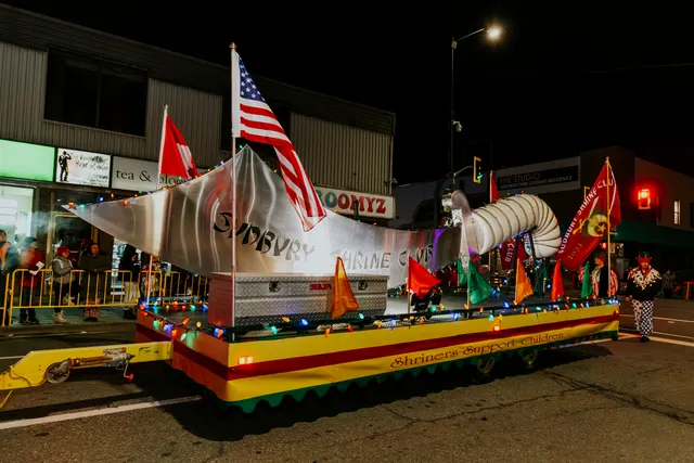 A silver whale-shaped float flying Canadian and American flags carries a banner reading Shriners Support Children.