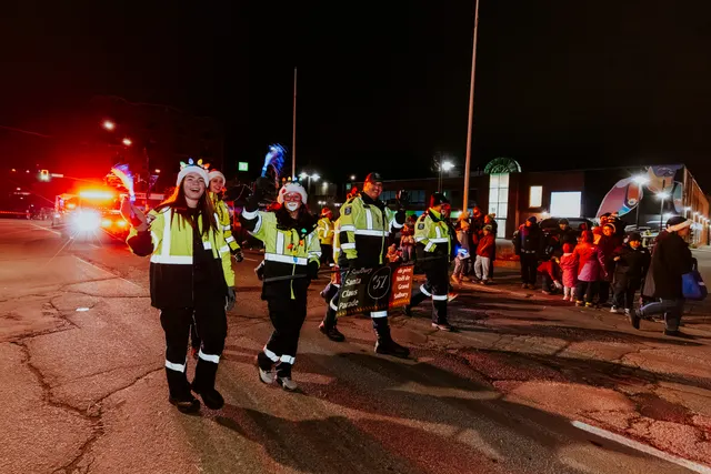 Marshals in high-visibility jackets and Santa hats wave while walking beside a fire truck.