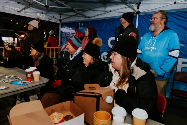 People sit at tables under a tent enjoying coffee and pastries during the parade.