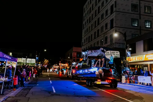 A narwhal-shaped float lit with blue lights carries a sign referencing Buddy the Elf down the street.