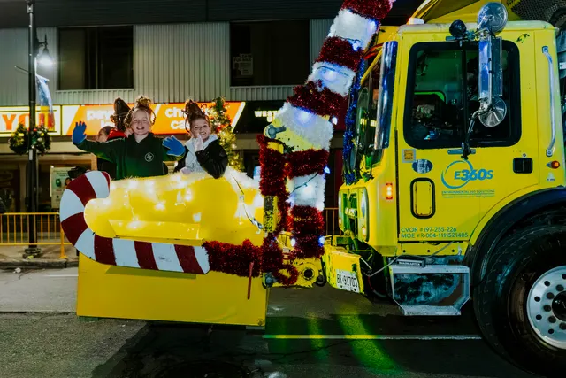 Two children wave from a candy-cane-shaped seat mounted on a decorated E360S service truck.