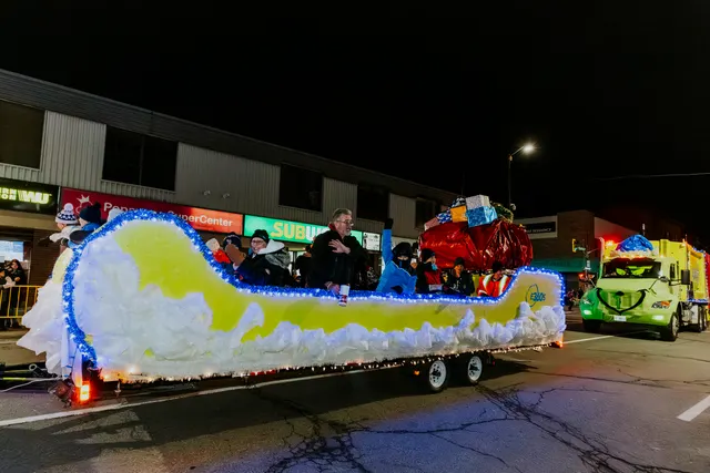 Riders wave from a sleigh-shaped float trimmed with lights and wrapped gifts.