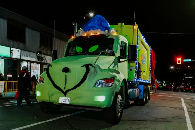 A green transport truck decorated as the Grinch's face leads a float down the street.