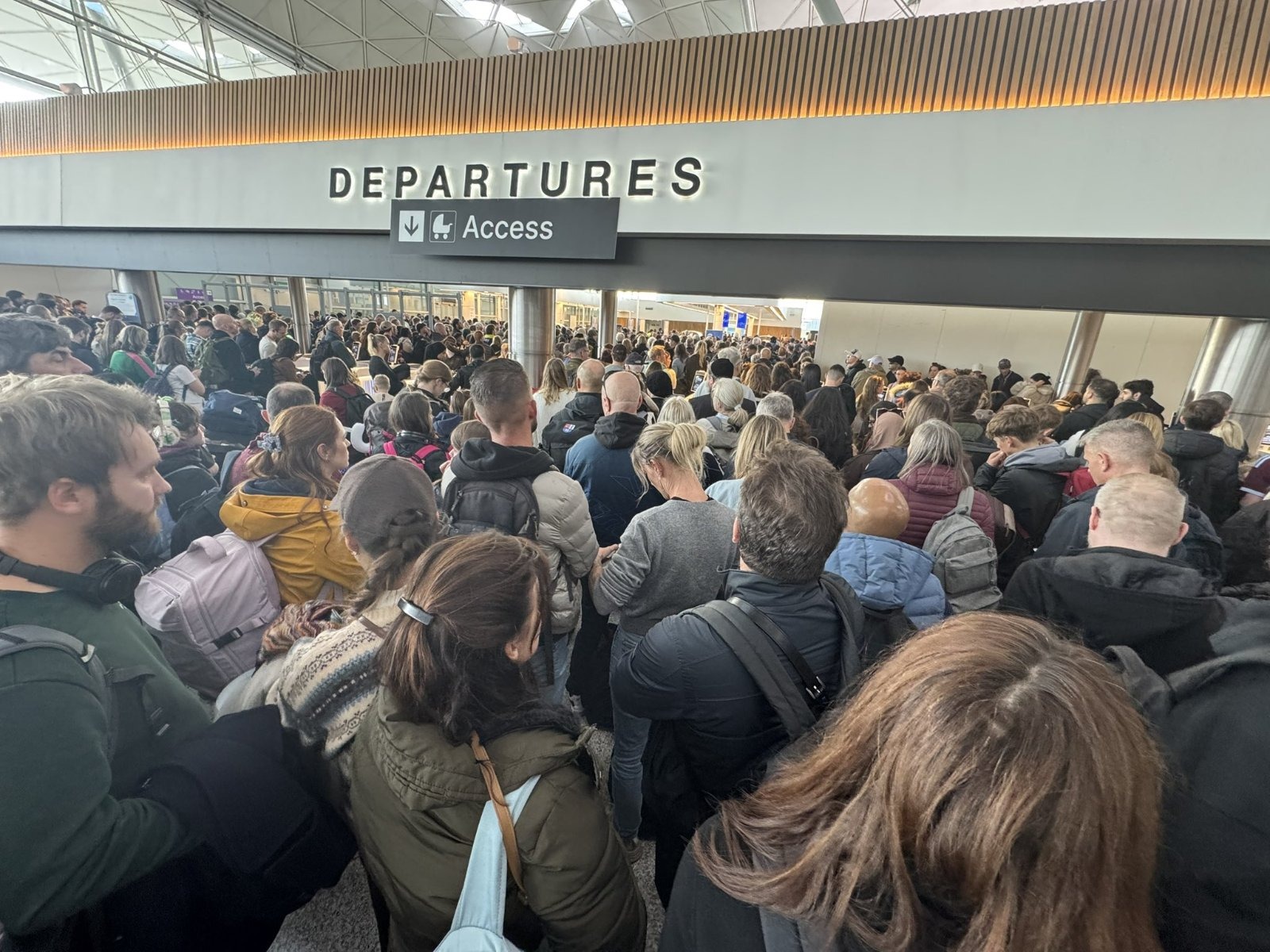Passengers crowding the departures hall at Stansted Airport, where security and baggage systems remain below full capacity after a power surge, with arrivals also left crammed on escalators awaiting passport control.