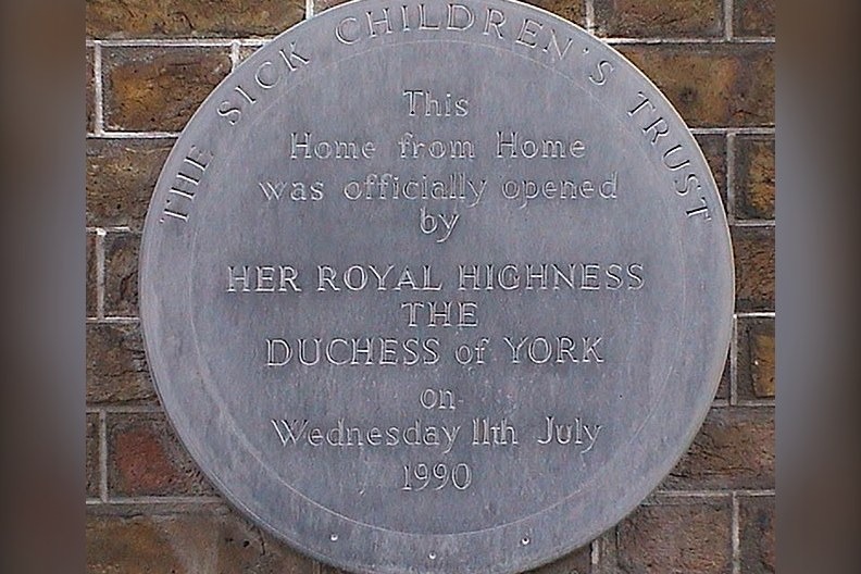 The grey slate plaque with gold lettering marking Sarah Ferguson's 1990 opening of a Sick Children's Trust hostel near Great Ormond Street Hospital, leaving only drill holes and an outline in the brickwork where it once…