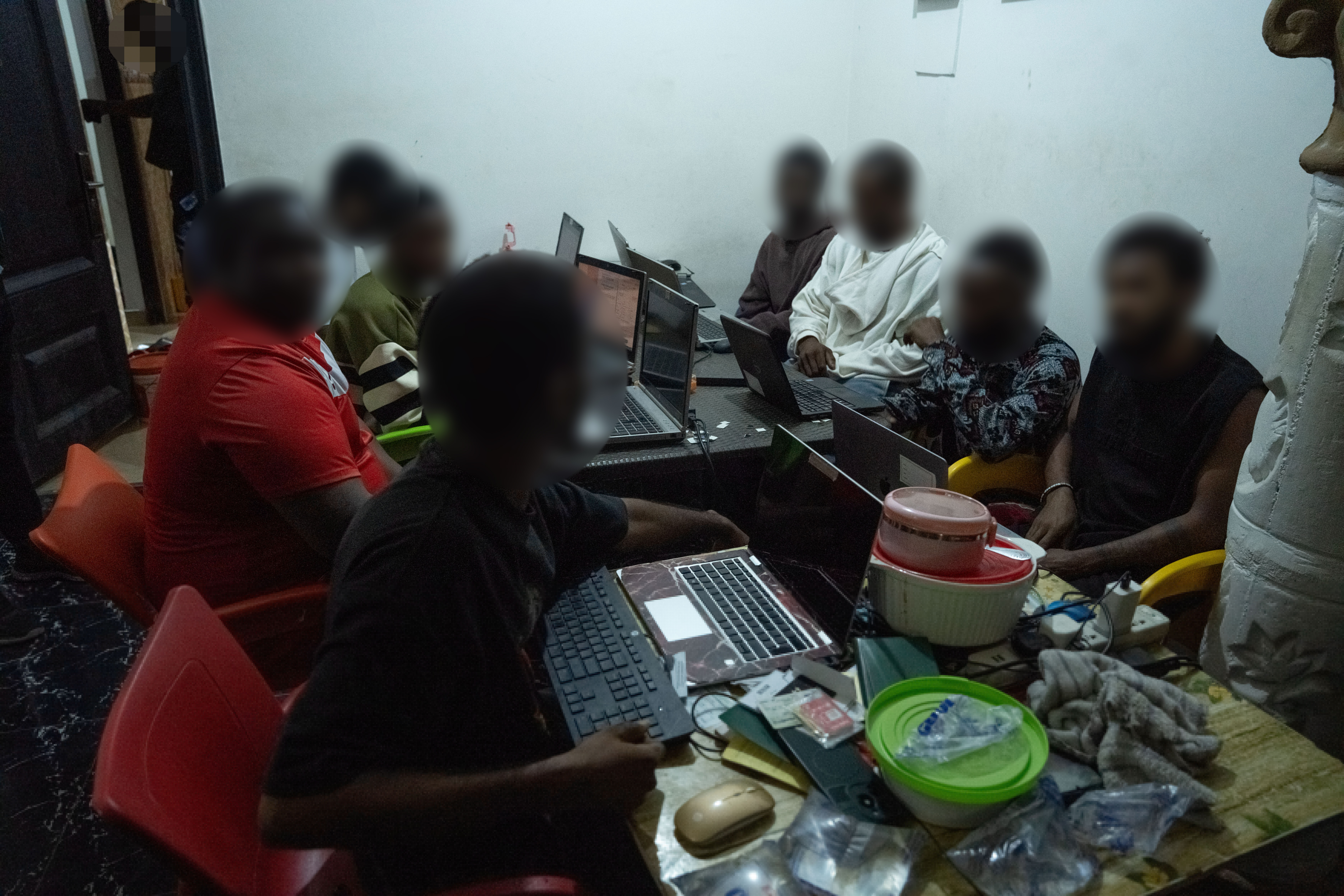Men with obscured faces at laptops inside a suspected scam compound in Ghana's Sasaabi area, where 19 people were arrested and 303 devices seized during Operation Blackout.