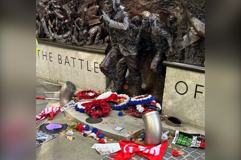 Poppy wreaths and protest placards at the base of the Battle of Britain Memorial on Victoria Embankment, where Revolutionary Communist Party activists climbed the monument, waving flags and a banner reading…