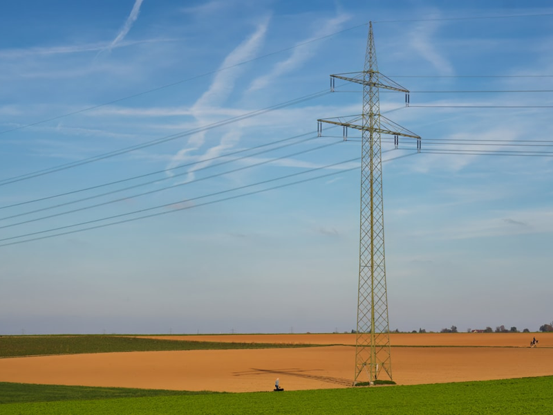A huge electricity pole on an brown agriculture field,shot from a public place.