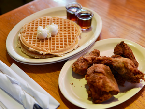 A classic serving of chicken and waffles at Roscoe’s House of Chicken and Waffles in Anaheim, California. This mouthwatering meal features golden, crispy fried chicken paired with fluffy waffles, topped with scoops of butter and served with sweet maple syrup on the side. Captured on a warm wooden table, this image embodies the comforting, indulgent flavors of soul food and Southern cuisine. A perfect representation of a beloved American brunch tradition, blending sweet and savory for the ultimate comfort food experience.