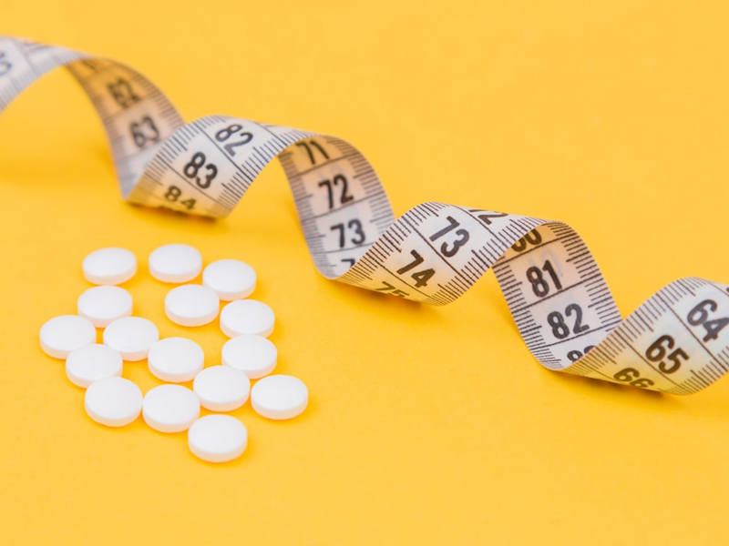 White measuring tape with a white pills, white vitamin on a yellow background. Diet. Slimming. Obesity. Place for an inscription. Weight loss marathon. Advertising. Top view. The close plan.
