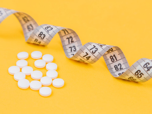 White measuring tape with a white pills, white vitamin on a yellow background. Diet. Slimming. Obesity. Place for an inscription. Weight loss marathon. Advertising. Top view. The close plan.