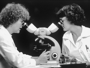 Two Caucasian women scientists looking through a double-headed microscope.