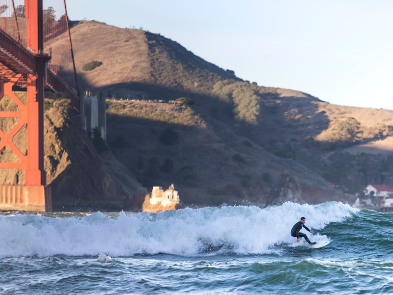 Surfer rides a wave near the golden gate bridge