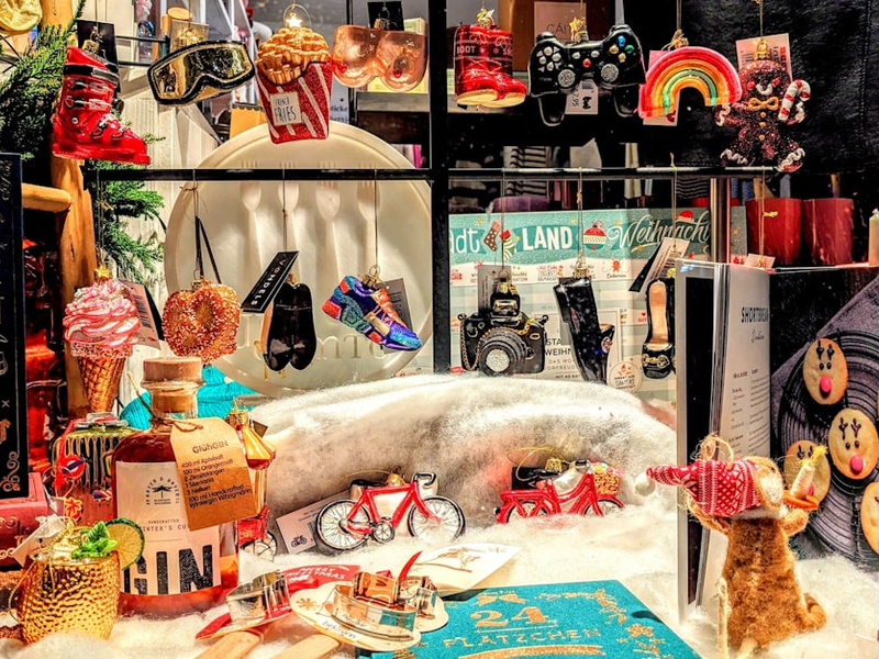 A cheerful and festive Christmas-themed shop window display featuring a mix of colorful Christmas ornaments and holiday decorations, showcasing festive treats, winter drinks, and playful gift ideas perfect for the holiday season.