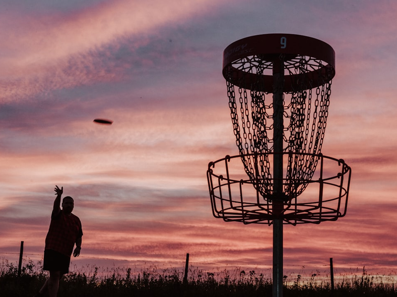 A silhouette of a man throwing a frisbee at a frisbee golf