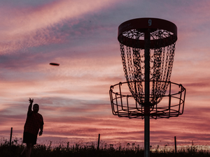 A silhouette of a man throwing a frisbee at a frisbee golf