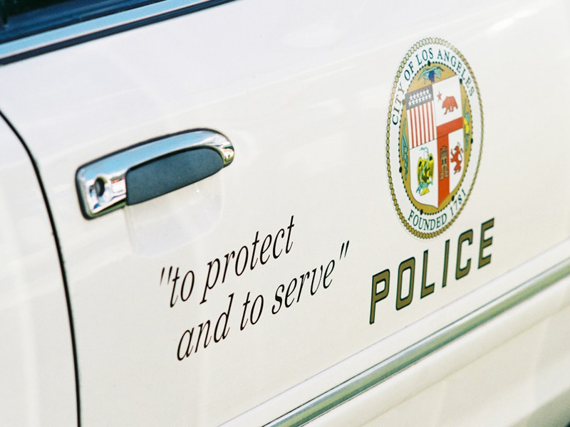 The door of an American police car. It has the symbol of Los Angeles and the line "to protect and to serve" on the side. Shot on film.