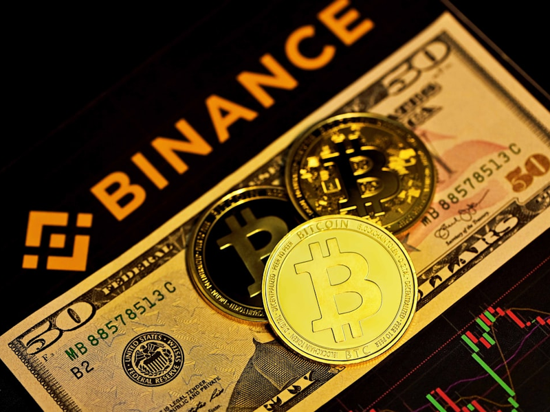 Three bitcoins on top of a $50 bill with the binance logo.