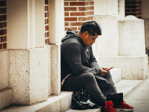 a man sitting on a sidewalk looking at his phone