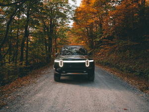 Forest Green Rivian R1T electric truck driving on a gravel road in the blue ridge mountains during fall