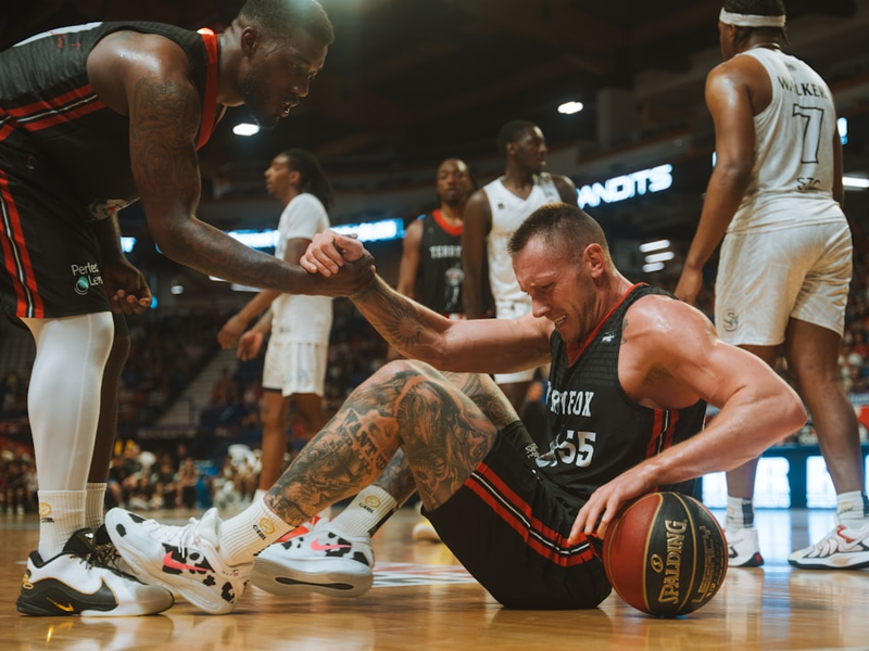 A basketball player helps his teammate up from the floor.