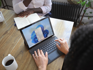Overhead view of two people at a table working with a Microsoft laptop and notebook
