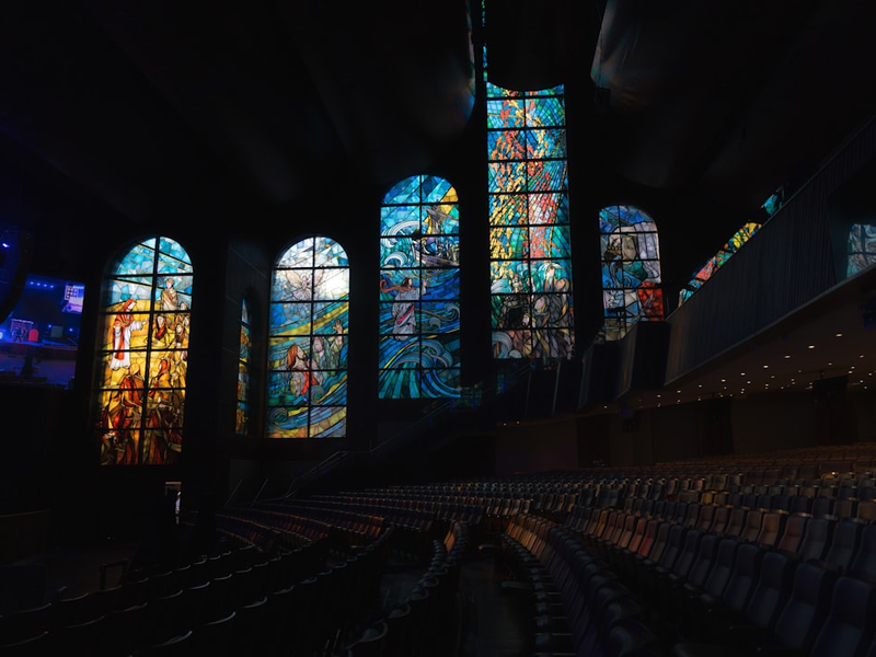 Colorful stained glass windows light up a dark auditorium.