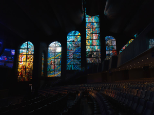 Colorful stained glass windows light up a dark auditorium.