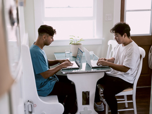 2 boys sitting on chair using laptop computers