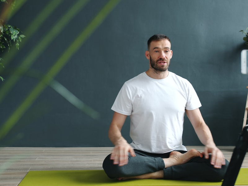 Yoga instructor in sportswear is teaching online recording tutorial in studio with smartphone speaking doing asana showing namaste gesture. People and sports concept.