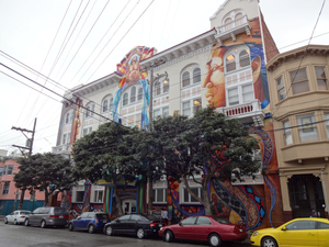 Building with colorful mural art and parked cars.