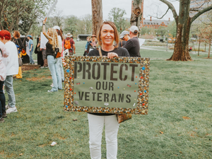 Woman protests to protect veterans with sign.