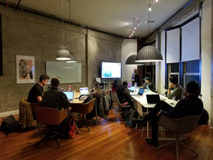 group of adult students sitting at a large table working on computers and discussing 