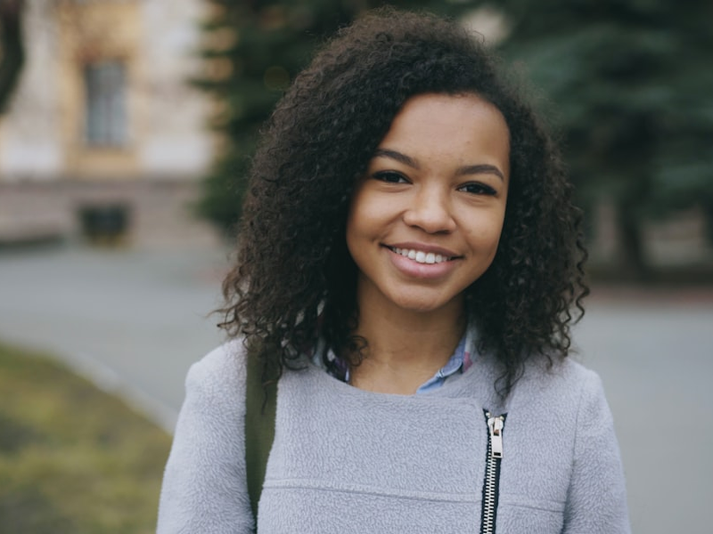 Portrait of mixed race curly student woman smiling into camera and laughing at city street