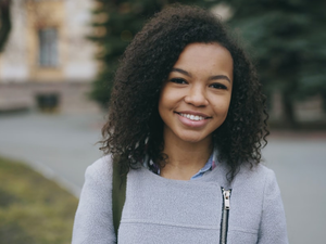 Portrait of mixed race curly student woman smiling into camera and laughing at city street