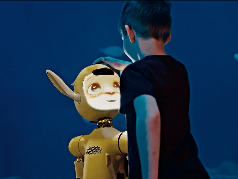 A young boy gently pats a yellow robot's head.