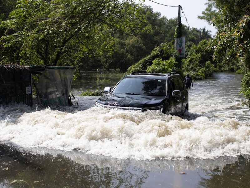 A black suv drives through a flooded street.