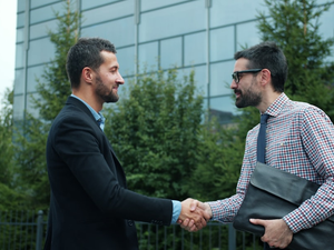 Business partners handsome young men are meeting outdoors in city shaking hands greeting saying hello enjoying partnership and cooperation. People and job concept.