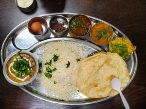 This is a thali, a traditional Indian meal consisting of a variety of dishes served on a large, round platter. The dishes typically include a selection of vegetarian and non-vegetarian curries, lentils, rice, bread (chapati), pickles, chutneys, yogurt, and dessert. Thali is a popular meal in India and is often served in restaurants and homes during special occasions or festivals.
