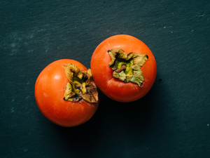 Two juicy ripe persimmons on a black slate